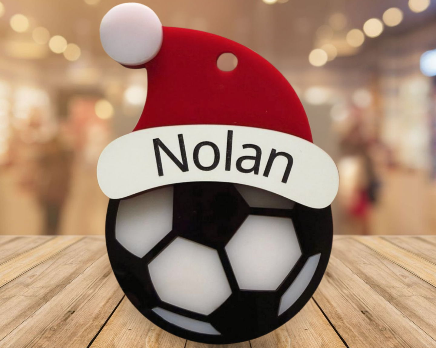 Soccer ball with a Santa hat and 'Nolan' text on a wooden surface with a blurred background